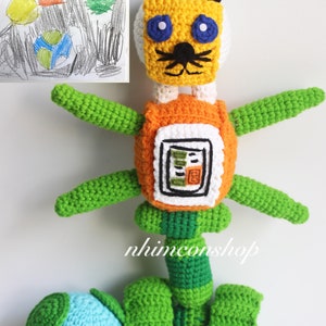 May include: A crocheted stuffed toy resembling a robot with a tiger head, orange and white body, green arms and legs, and a blue sphere for a foot. The toy is standing next to a drawing of a similar robot.