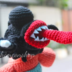 Puede incluir: Mu&ntilde;eco monstruo de ganchillo con cabeza negra, boca y lengua rojas y dientes blancos. El mu&ntilde;eco tiene brazos negros con detalles blancos y negros. El texto "nhimconshop" es visible en el mu&ntilde;eco.