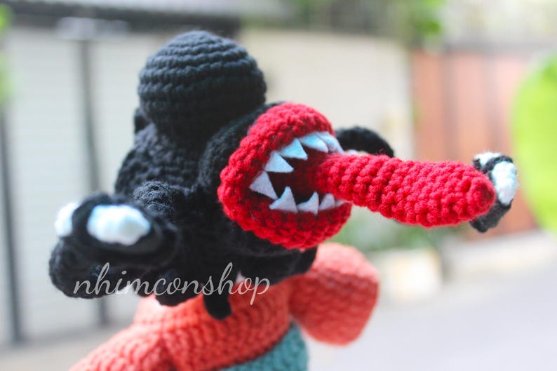 Puede incluir: Mu&ntilde;eco monstruo de ganchillo con cabeza negra, boca y lengua rojas y dientes blancos. El mu&ntilde;eco tiene brazos negros con detalles blancos y negros. El texto "nhimconshop" es visible en el mu&ntilde;eco.