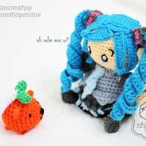 May include: A blue crocheted doll with long blue hair and a gray dress. The doll is holding a small orange crocheted pumpkin with green leaves. The doll is looking at the pumpkin and saying "eh who are u?"