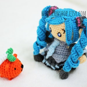 May include: A crocheted blue-haired doll with a white and blue scarf and a crocheted orange pumpkin with green leaves.