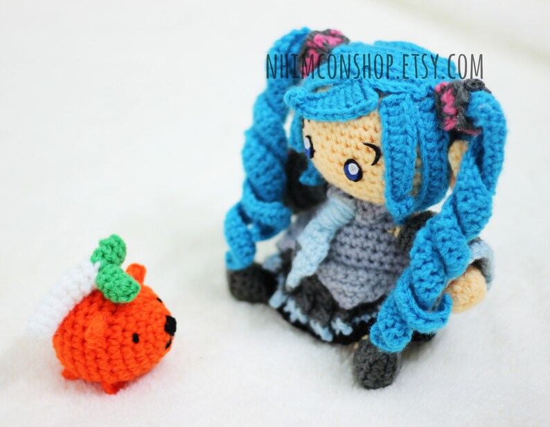 May include: A crocheted blue-haired doll with a white and blue scarf and a crocheted orange pumpkin with green leaves.
