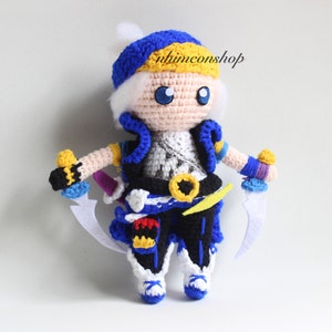 May include: Crocheted plush toy of a character with white hair, blue and yellow clothing, and a blue hat. The character is holding two white swords.