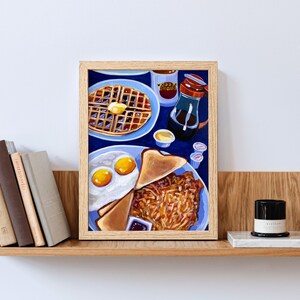 May include: A framed painting of a breakfast plate with eggs, toast, and hash browns, alongside a waffle with butter, syrup, and coffee. The painting is set against a blue background, with a wooden frame.