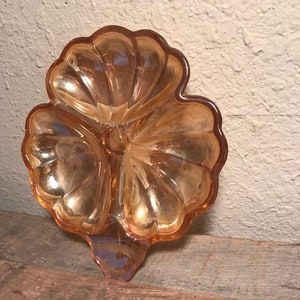 Puede incluir: Un plato de vidrio vintage, iridiscente, de tres secciones, con forma de flor. El plato es de color melocotón pálido con un acabado brillante.