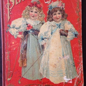 Op de afbeelding: Vintage boekcover "Playday Stories". Rode achtergrond met gouden titel. Twee meisjes in pasteljurken, een met golfclub. Onderdeel van de "Sunbeam Series". Het boek vertoont tekenen van ouderdom.