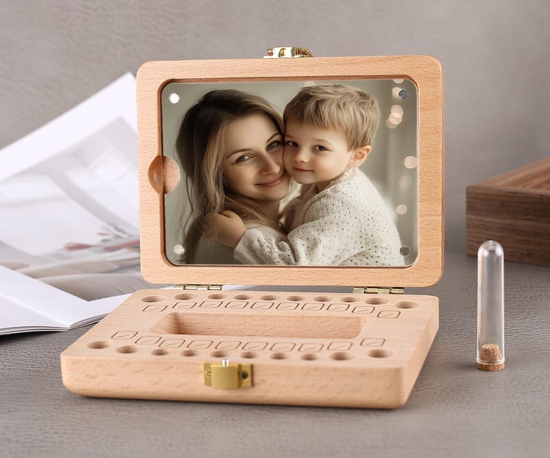 May include: A wooden baby tooth keepsake box with a hinged lid and a clear acrylic window displaying a photo of a mother and child. The box has individual slots for each tooth and a small glass vial.