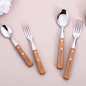 May include: A set of four stainless steel utensils with light brown wooden handles. Two pieces feature the text "Fondue" and two pieces feature the text "Enjoy your meal" engraved on the handles, which are secured with two silver rivets.