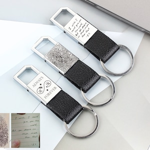 Puede incluir: Tres llaveros plateados con correas de cuero negro. Los llaveros presentan mensajes grabados, incluyendo "Always Forever" con un corazón y un símbolo de infinito, y un diseño de huella digital. Un llavero tiene el texto "I wish I could give you the world, but you deserve so much more than that -J.T."