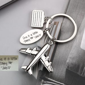 May include: Silver airplane keychain with a luggage charm and a tag that says "Give it a little tappy tap - Jules".