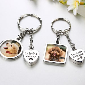 Puede incluir: Dos llaveros de foto plateados con un dije en forma de corazón. El primer dije presenta una foto de un cachorro golden retriever. El segundo dije presenta una foto de un caniche marrón. El dije en forma de corazón tiene el texto "In loving memory" y huellas de patas. El dije en forma de corazón del segundo llavero tiene el texto "Sep 08, 2008 Oct 15, 2022" y huellas de patas.