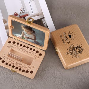 May include: Wooden baby tooth keepsake box with a hinged lid. The lid has a photo of a child. The box is open, revealing spaces for baby teeth and a small vial. The closed box is engraved with "Peggy's First Teeth" and a fairy illustration.