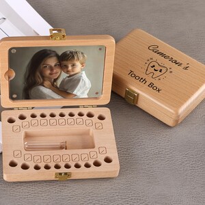 May include: Wooden tooth box with a hinged lid, featuring a photo of a mother and child. The open box reveals spaces for baby teeth and a small vial. The closed lid is engraved with "Cameron's Tooth Box".