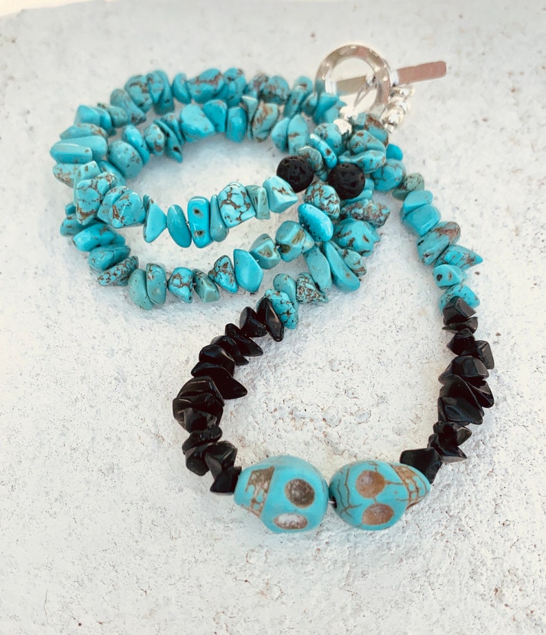 May include: A layered necklace featuring turquoise chip beads and black onyx chips. The necklace includes two turquoise skull beads and a silver toggle clasp. The turquoise beads have brown matrix patterns.