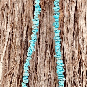 May include: A turquoise chip bead necklace with black onyx accents and a skull bead design. The necklace is displayed against a textured, brown background.