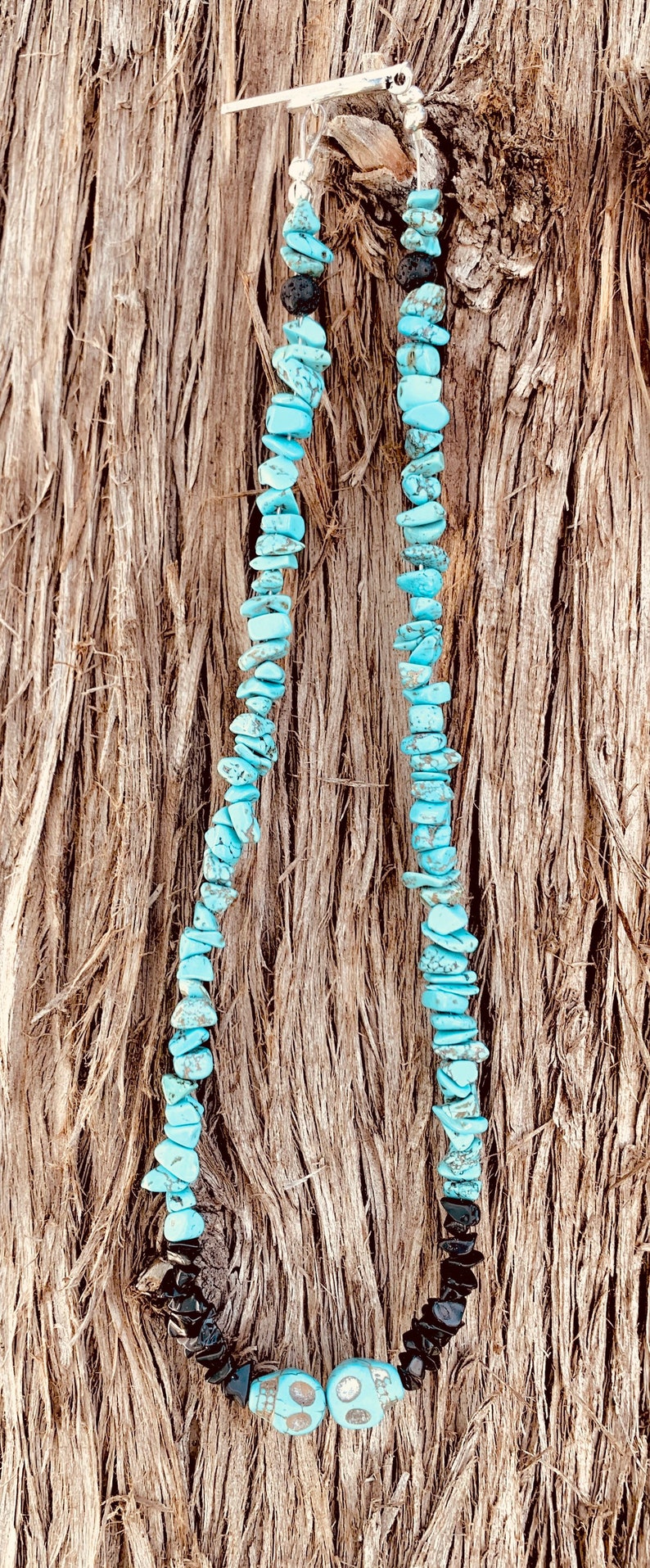 May include: A turquoise chip bead necklace with black onyx accents and a skull bead design. The necklace is displayed against a textured, brown background.