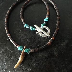 Peut inclure: Un collier de perles brun et noir avec un accent en pierre turquoise et un pendentif en os. Le collier a un fermoir à glissière argenté.