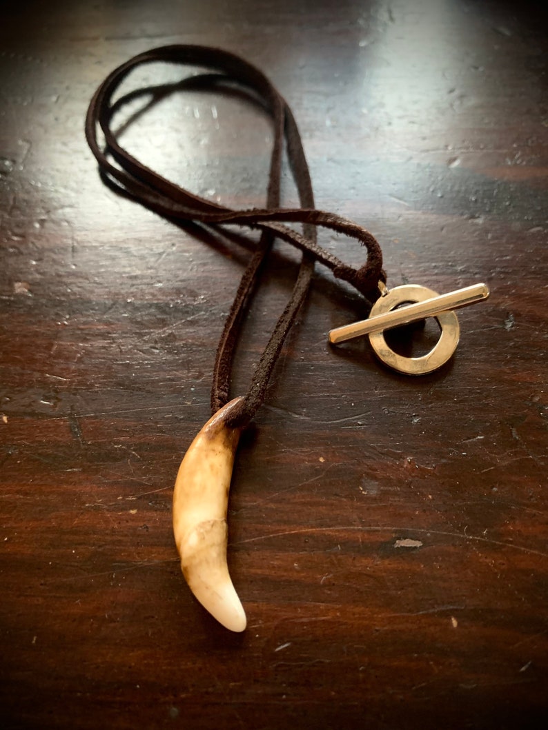 May include: A brown leather cord necklace with a silver toggle clasp and a white tooth pendant.