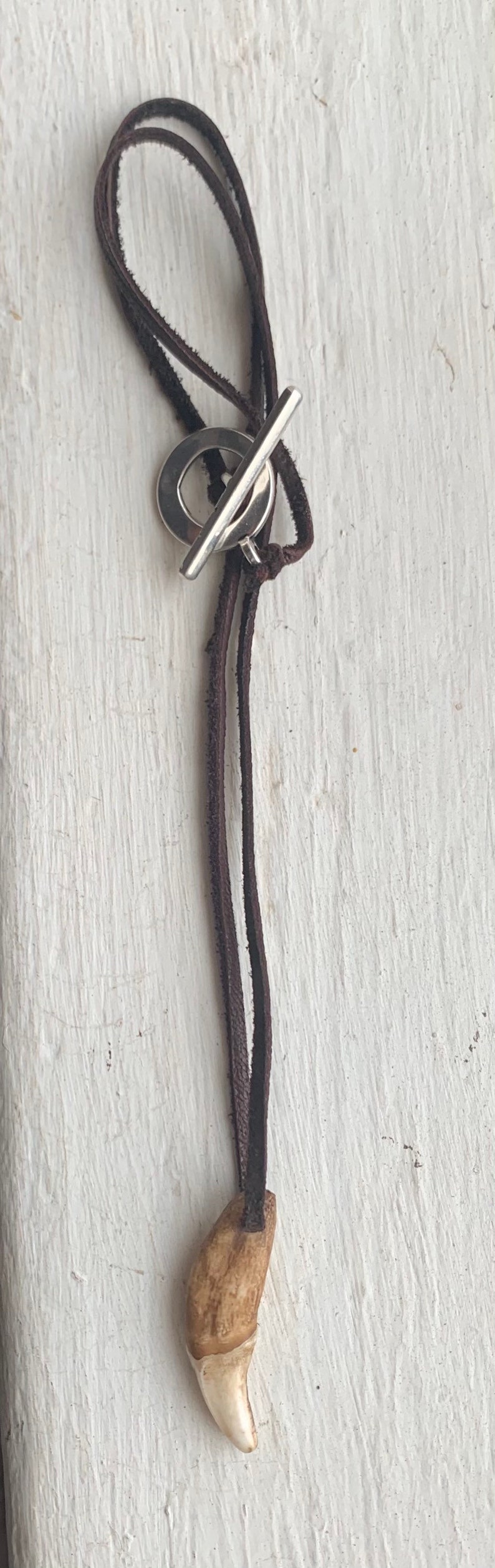 May include: A brown leather cord necklace with a silver toggle clasp and a brown and white tooth pendant.