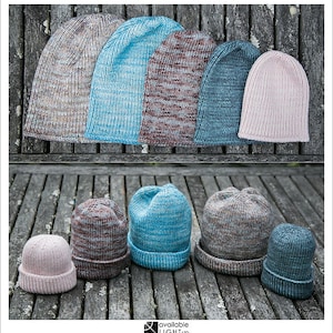 Può includere: Una collezione di otto berretti a maglia in vari colori e motivi, tra cui blu, rosa, marrone e grigio. I berretti sono disposti in due file su una superficie di legno.