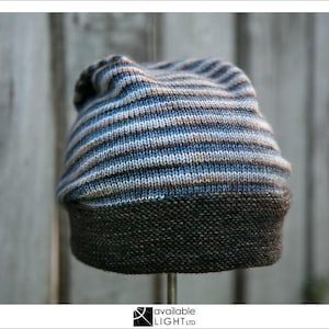 May include: A striped knit beanie hat with a brown brim. The hat is made of a soft, textured yarn and has a casual, comfortable style.