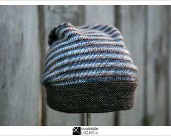Puede incluir: Un gorro de punto a rayas con un borde marrón. El gorro está hecho de un hilo suave y texturizado y tiene un estilo informal y cómodo.