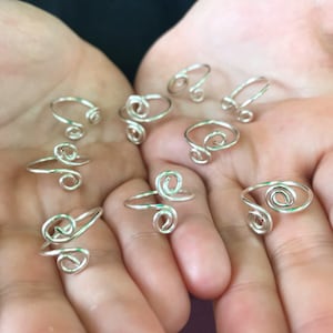Puede incluir: Una colección de anillos de alambre de plata con un diseño en espiral. Los anillos se muestran en las manos abiertas de una persona.