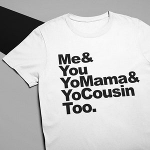 Op de afbeelding: Wit t-shirt met de tekst "Me & You YoMama & YoCousin Too" in vette zwarte letters. Het shirt heeft korte mouwen en is gemaakt van een zacht materiaal. De achtergrond is een mix van grijs en zwart.