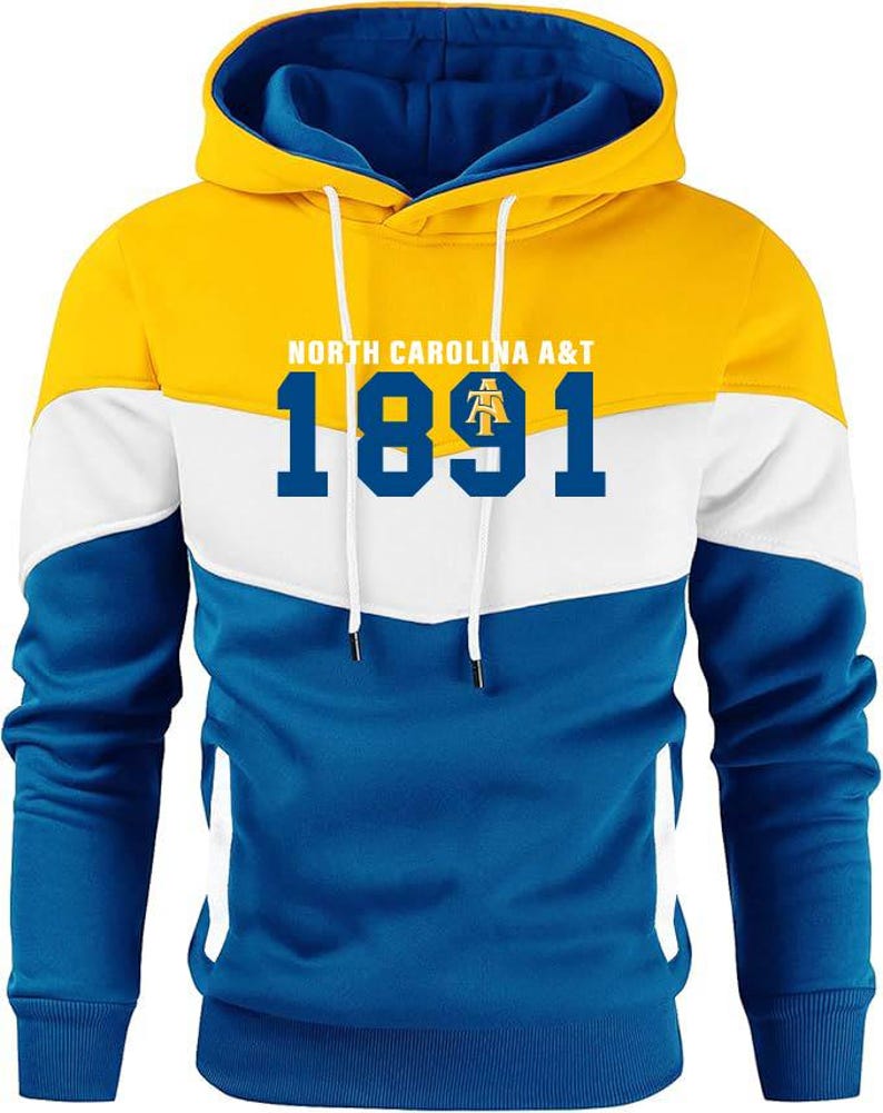 Puede incluir: Una sudadera con capucha en amarillo, blanco y azul con el texto "NORTH CAROLINA A&T" y el n&uacute;mero "1891" en azul marino. La sudadera tiene un cord&oacute;n y un bolsillo tipo canguro.