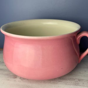 May include: A pink ceramic chamber pot with a white interior and a single handle.