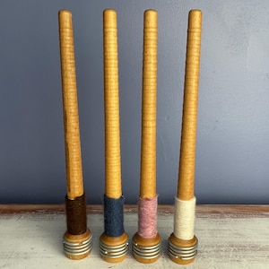 May include: Four wooden spools with different colored yarn wrapped around them. The spools are all the same size and shape, and they have a metal ring at the bottom.
