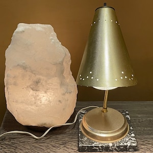 May include: A gold table lamp with a perforated shade and a white salt lamp on a wooden surface.