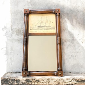 May include: A rectangular wooden mirror with a dark brown frame. The top section features a sepia-toned print of a clipper ship, with the text "CLIPPER SHIP. NIGHTINGALE". The lower section is a reflective mirror. The frame has decorative turned posts.