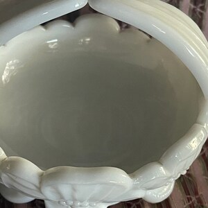 May include: A white milk glass bowl with a scalloped rim and a handle. The bowl has a floral design and is in excellent condition.