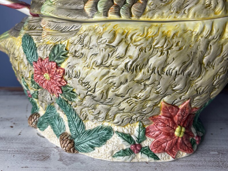 May include: A ceramic Christmas serving bowl shaped like a bird with a candy cane in its beak. The bowl is decorated with poinsettia flowers, holly, and pine branches.