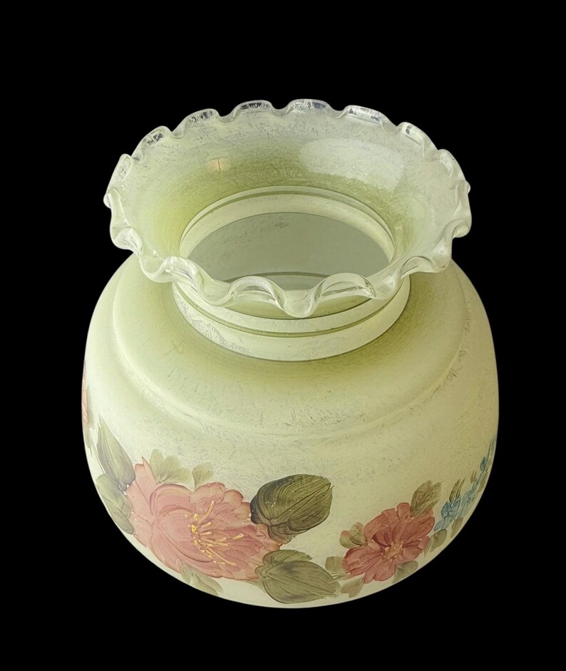 Puede incluir: Una pantalla de l&aacute;mpara de vidrio verde p&aacute;lido vintage con un borde con volantes. La pantalla de la l&aacute;mpara presenta dise&ntilde;os florales pintados a mano en tonos de rosa, rojo y azul, con hojas verdes. El vidrio tiene una apariencia texturizada y el fondo es negro.