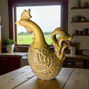 May include: A large, decorative rooster statue in shades of yellow and gold, with intricate embossed patterns. The rooster is positioned on a wooden table, with a window and a green field with chickens in the background. A unique home decor item.