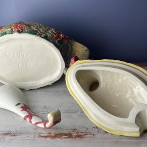 May include: A ceramic turkey-shaped serving dish with a ladle. The dish is decorated with green, red, and yellow floral designs. The bottom of the dish has the text "1997 YH".