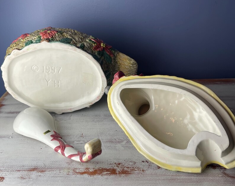 May include: A ceramic turkey-shaped serving dish with a ladle. The dish is decorated with green, red, and yellow floral designs. The bottom of the dish has the text "1997 YH".