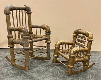 May include: Two rocking chairs made of gold painted metal pipe. The larger chair has a slatted back and the smaller chair has a woven back.