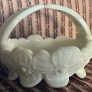 May include: White milk glass basket with a handle and floral design. The basket is shaped like a flower with a scalloped edge.