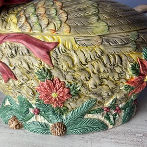May include: A ceramic goose serving dish with a detailed, textured design. The goose is decorated with a red ribbon, green leaves, and red poinsettia flowers.