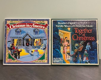 May include: Two vintage Christmas albums. The album on the left is titled "Christmas in America" with a snowy house illustration. The album on the right is "Reader's Digest Family Album of Christmas Music Together at Christmas" with a family illustration.
