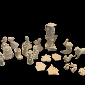 May include: A collection of unpainted ceramic figurines, including angels, a bell, a boot, Santa figures, a graduate, a mushroom, a dog, a squirrel, and various other shapes. The figurines are all in a neutral, off-white color.