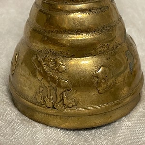 May include: A brass bell with a detailed design of a moose and other animals. The bell has a rounded shape and a textured surface.