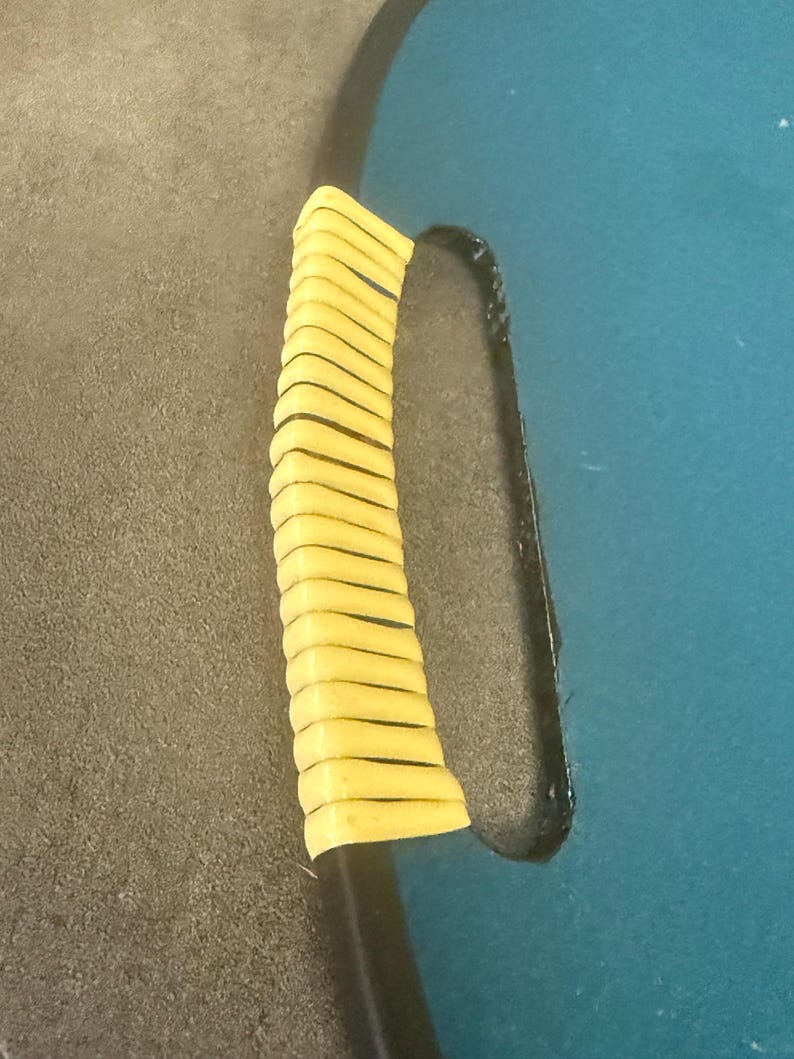 May include: Close-up of a black handle with a yellow grip. The handle is attached to a teal blue surface. The grip is made of multiple yellow, horizontal, rectangular pieces.