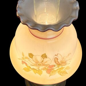 May include: A vintage-style table lamp with a floral design. The lamp features a cream-colored shade adorned with peach and yellow flowers and green leaves. The base is a brass color, and the lamp has a clear glass chimney.