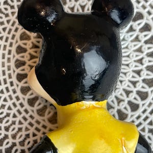 May include: A vintage ceramic figurine of Mickey Mouse. The figurine is painted black, yellow, and blue. Mickey is wearing a yellow shirt and blue pants.