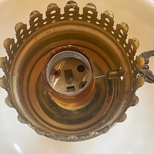 May include: Close-up of a gold-toned lamp socket with a decorative, scalloped edge. The socket has a standard light bulb base and a small, ornate metal handle.