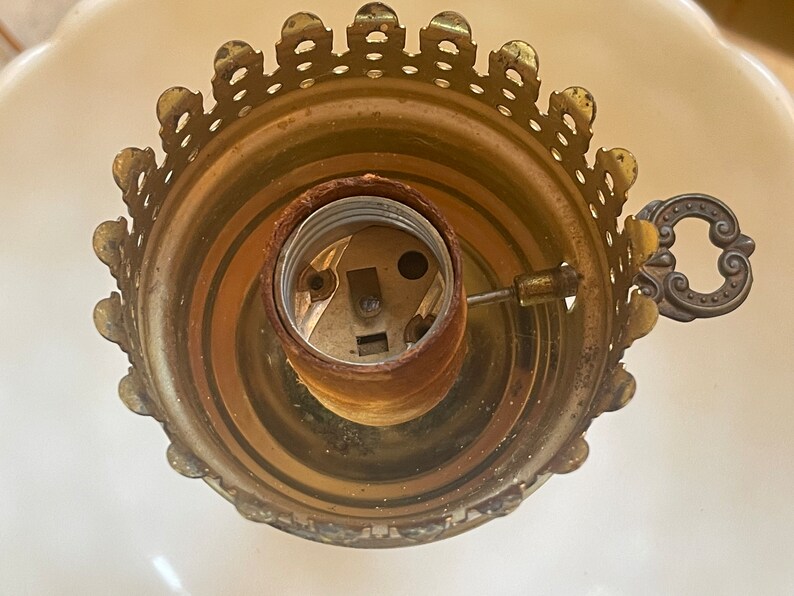 May include: Close-up of a gold-toned lamp socket with a decorative, scalloped edge. The socket has a standard light bulb base and a small, ornate metal handle.
